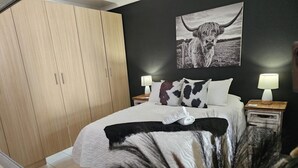 Un dormitorio con una cama, dos mesitas de noche con lámparas, un armario y un cuadro colgado en la pared.