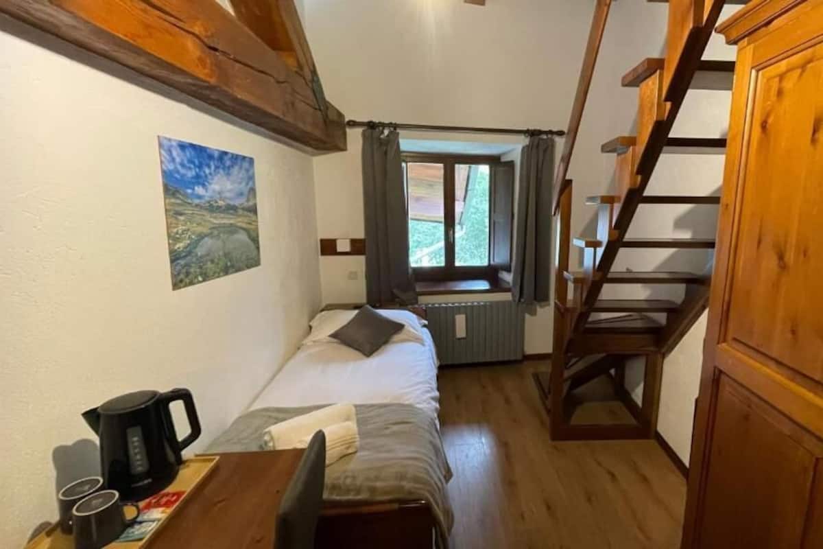 A bedroom with a bed, a window, a radiator, a wooden staircase, and a wooden cabinet.