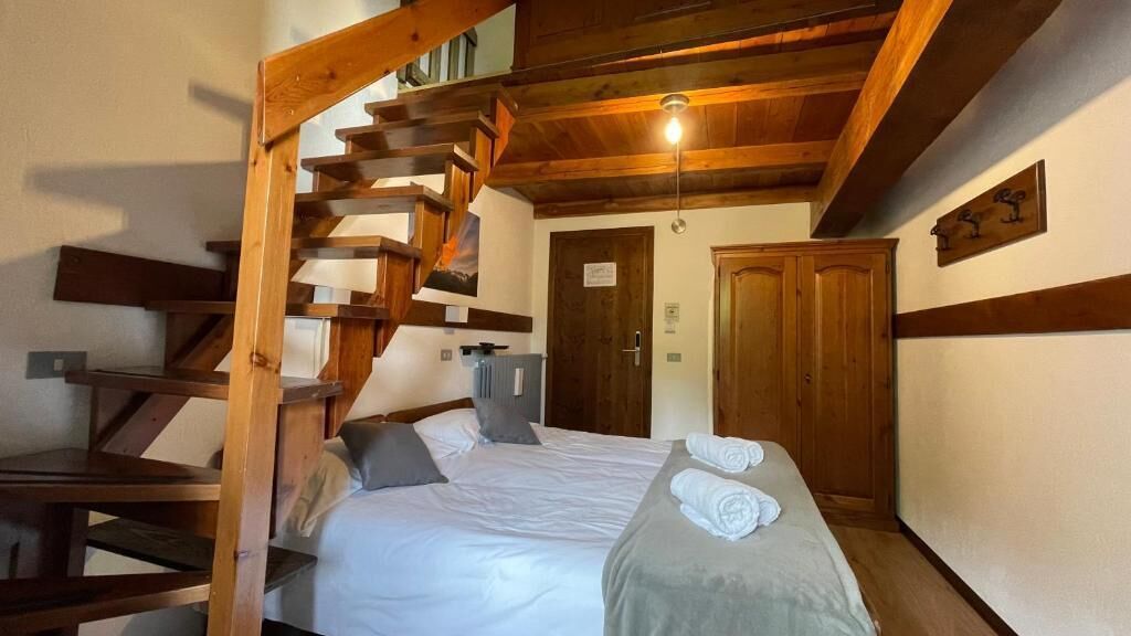 Um quarto com escada de madeira, cama com roupa de cama branca, porta de madeira e luminária no teto.