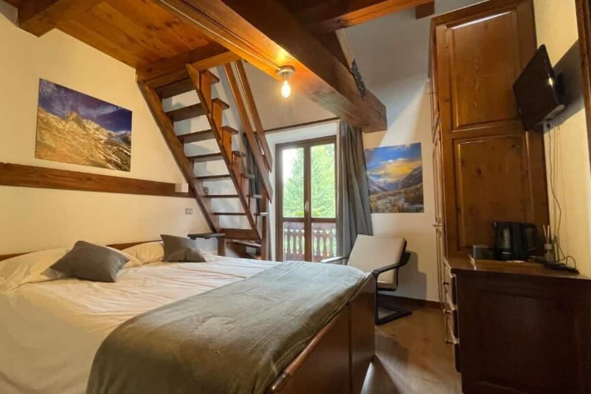 Une chambre à coucher avec un lit, un bureau en bois, une chaise, un escalier et une fenêtre.