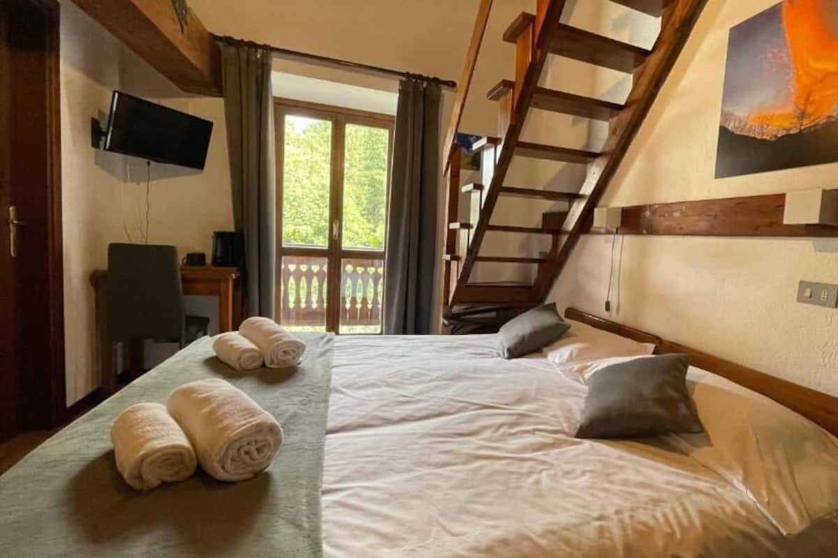 A bedroom with a bed, pillows, a TV, a desk, and a window with curtains.