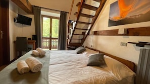 Un dormitorio con cama, almohadas, televisión, escritorio y ventana con cortinas.