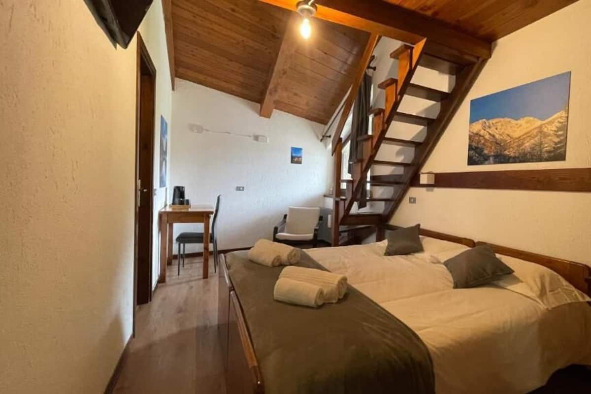 Une chambre à coucher avec un lit, un bureau, une chaise, un escalier et un tableau représentant une montagne accroché au mur.