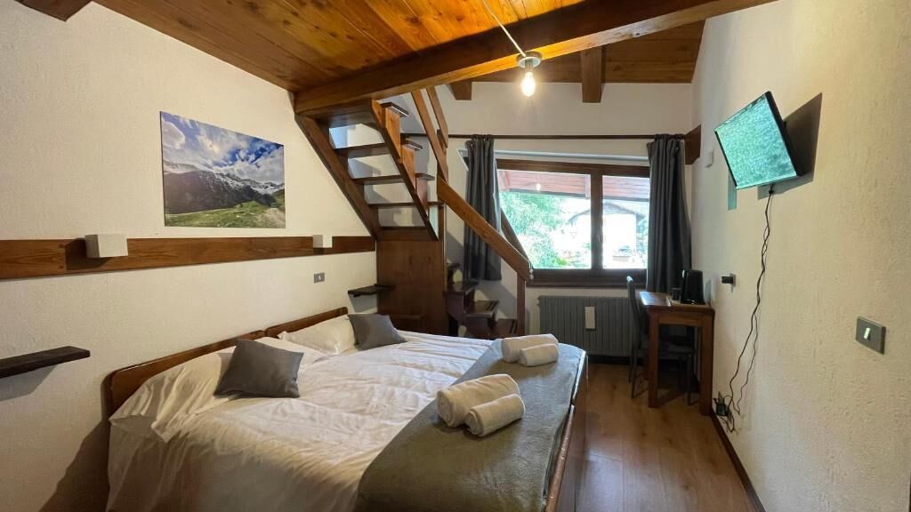 Quarto com cama, escrivaninha, televisão, janela e escada.