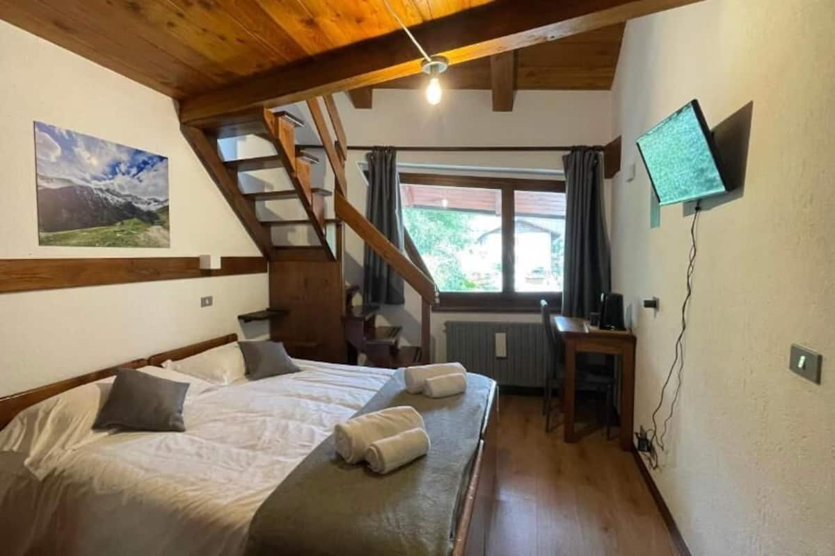 Une chambre à coucher avec un lit, un bureau, une télévision, une fenêtre et un escalier.