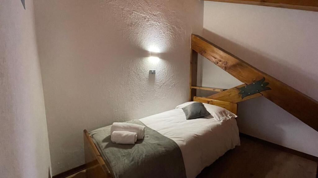 Ein kleines, gemütliches Schlafzimmer mit einem Einzelbett, einem Holzkopfende und einer schrägen Decke.