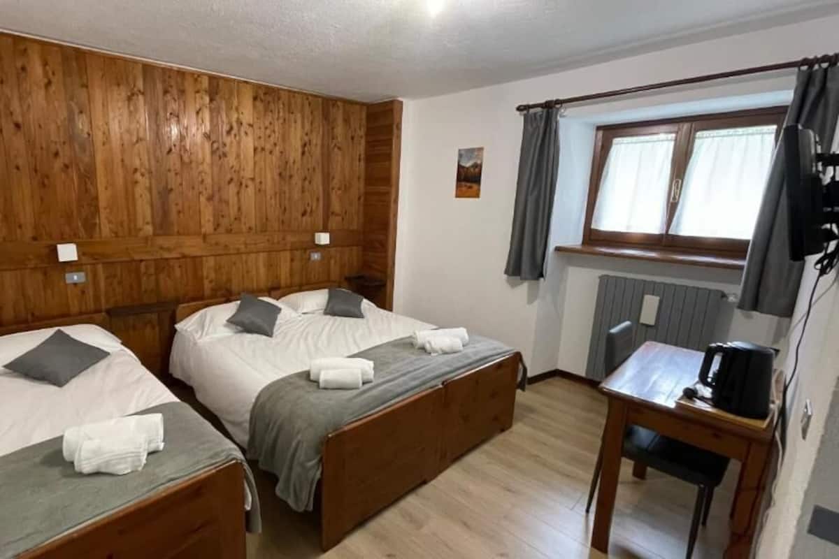 Une chambre avec deux lits en bois, une petite table avec une bouilloire et une fenêtre avec des rideaux.