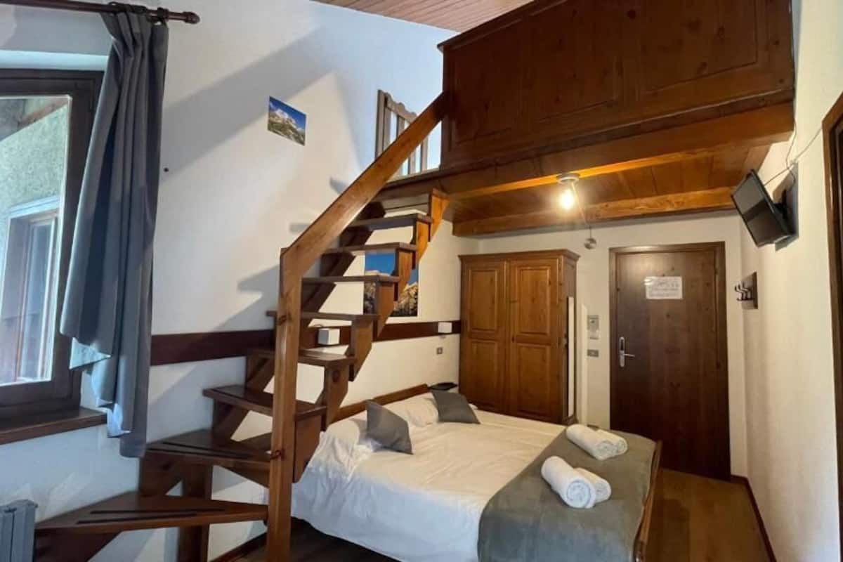 Une pièce avec un lit, un escalier en bois, une porte et une fenêtre.
