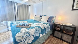 A bedroom with a bed, a nightstand, a lamp, and a window with curtains. - Delightful condo with AC in vibrant Honolulu perfect for your stay (Honolulu)