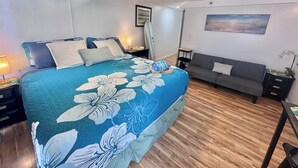 A bedroom with a bed, a nightstand, a lamp, a sofa, a picture on the wall, and a ceiling fan. - Delightful condo with AC in vibrant Honolulu perfect for your stay (Honolulu)