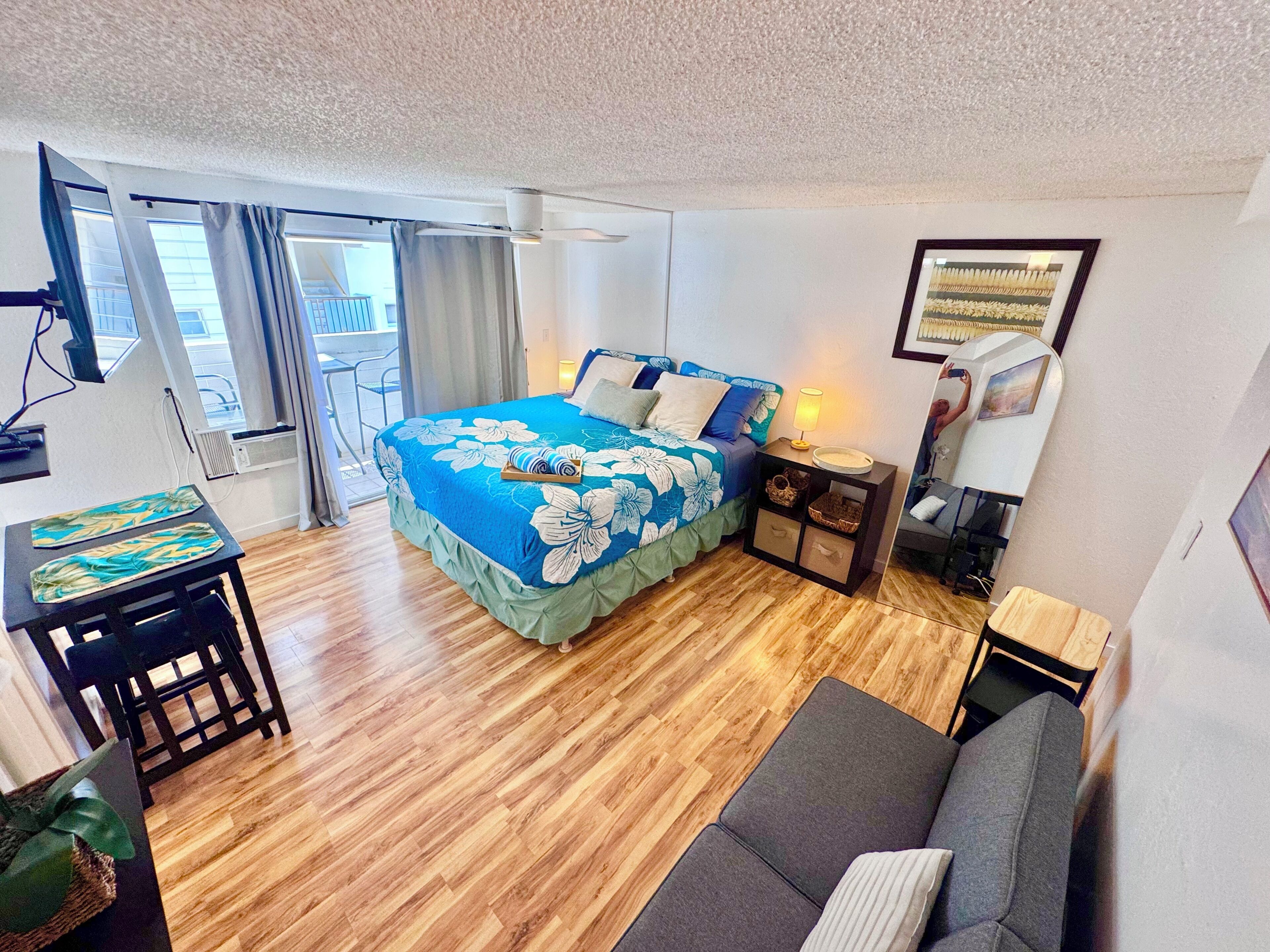 A hotel room with a bed, a desk, a chair, a sofa, a TV, and a window with curtains.
