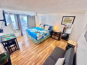 A hotel room with a bed, a desk, a chair, a sofa, a TV, and a window with curtains.