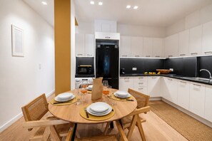 Eine moderne Küche mit weißen Schränken, einem schwarzen Kühlschrank und einem Essbereich mit einem Holztisch und Stühlen.