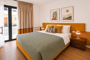 Ein Hotelzimmer mit Bett, Nachttisch, Lampe, einem Fenster mit Vorhängen und zwei Wandbildern.