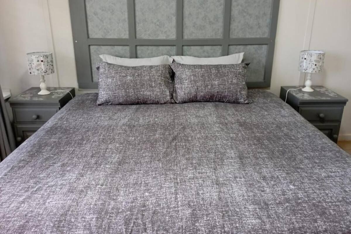 Una cama con colcha gris texturizada, dos almohadas grises y un cabecero gris.