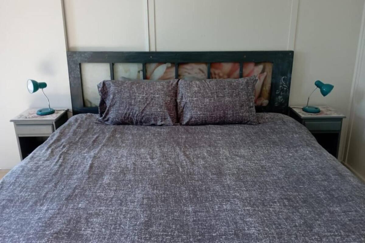 Una cama con cubrecama gris texturizado y dos almohadas, flanqueada por dos mesitas de noche con lámparas.