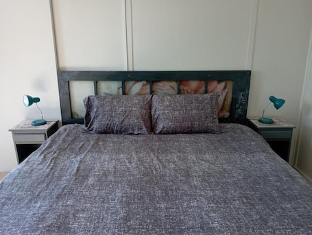A bed with a grey textured bedspread and two pillows, flanked by two bedside tables with lamps.. Eagles Nest Bed & Breakfast