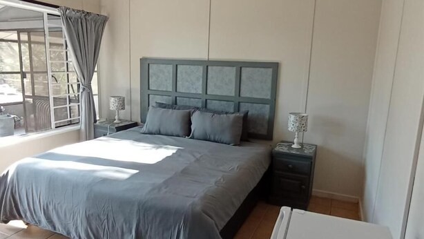 Une chambre à coucher avec un lit, des tables de chevet, une lampe et une fenêtre avec des rideaux.