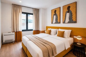 Ein Hotelzimmer mit Bett, Nachttisch, Lampe, einem Fenster mit Vorhängen und Bildern an der Wand.