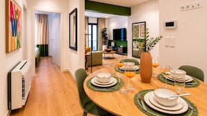 A dining area with a wooden table set for four, a large vase, and a television in the background. - LIV - Upscale Athenian Apartment 1C (Athens)