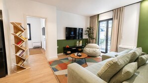 Un salon comprenant un canapé, une table basse, une bibliothèque, un téléviseur et une plante.