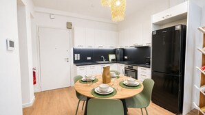 Une cuisine moderne avec un réfrigérateur noir, des placards blancs et une table à manger pour quatre personnes.