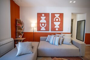 Ein modernes Wohnzimmer mit einem grauen Sofa, gestreiften Kissen, einem Bücherregal und abstrakter Wandkunst.