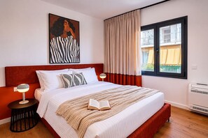 Ein Schlafzimmer mit einem Bett, einem Nachttisch mit Lampe, einem Fenster mit Vorhängen, einem Wandbild und einer Klimaanlage.
