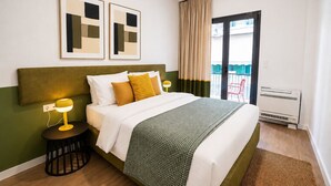Ein Hotelzimmer mit Bett, Nachttisch mit Lampe, einem Fenster mit Vorhängen und Blick auf einen Balkon.