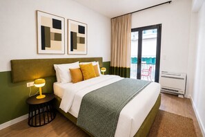 Ein Hotelzimmer mit Bett, Nachttisch mit Lampe, einem Fenster mit Vorhängen und Blick auf einen Balkon.
