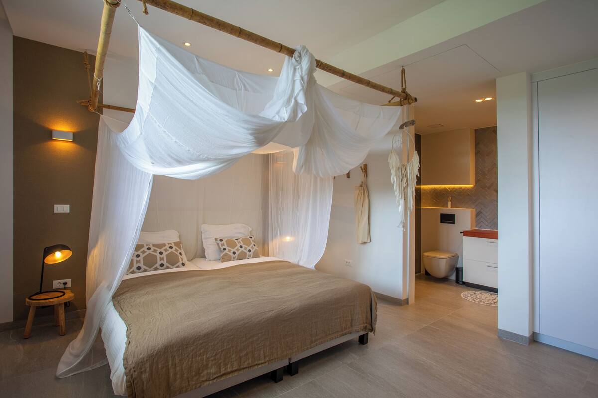 Un dormitorio con cama a dosel, lámpara de noche y vistas al baño.