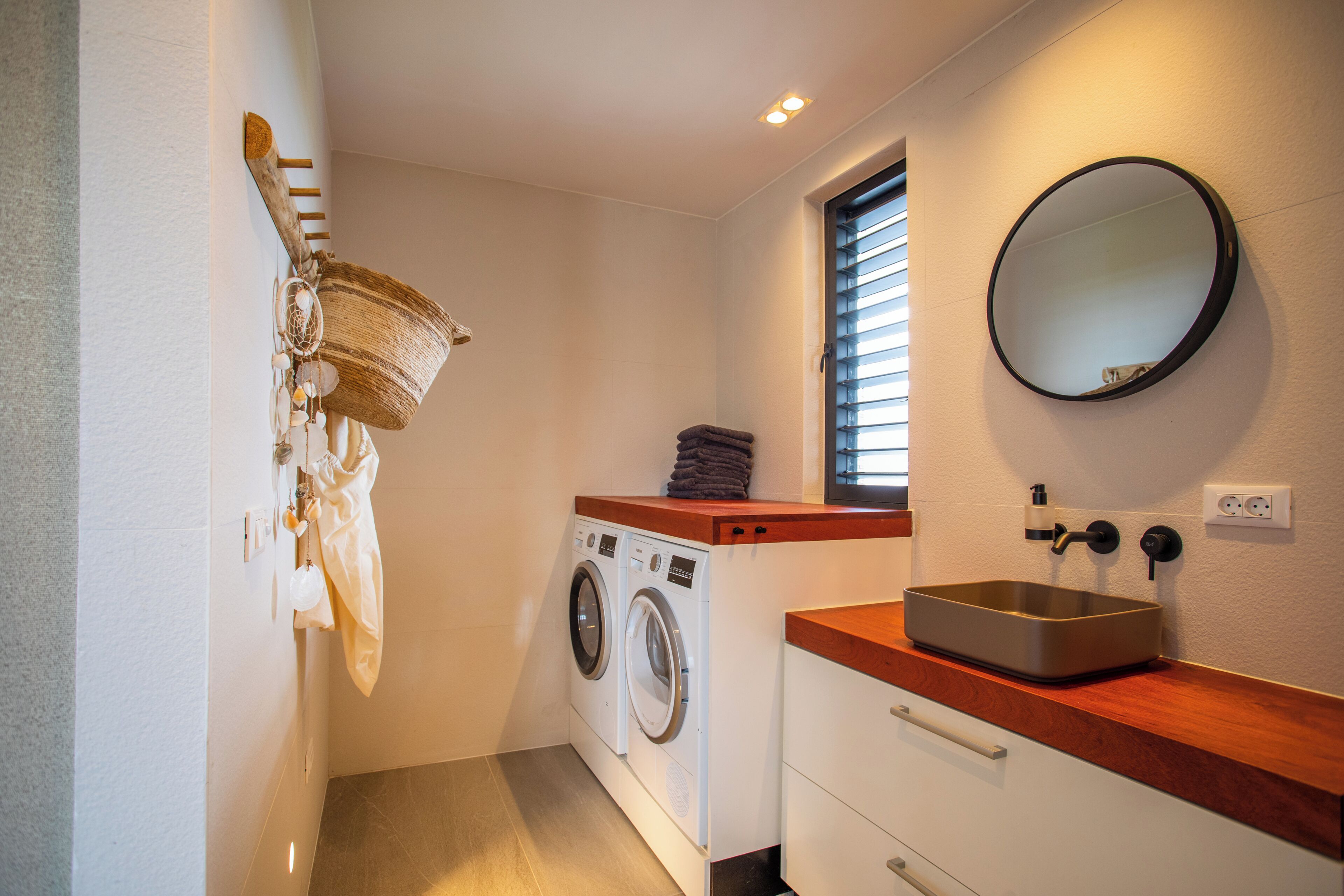 A compact laundry room with a washing machine, a sink, and a window with blinds.