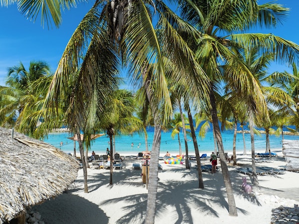A beach with palm trees, a thatched structure, and sun loungers. - The Shore - Blue Bay Golf & Beach Resort (Sint Michiel)