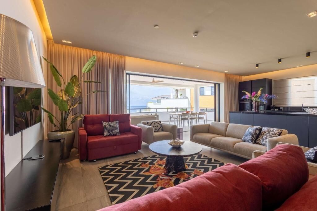 Una sala de estar moderna con sofás, una mesita de centro y un televisor. Tiene un balcón con vistas.