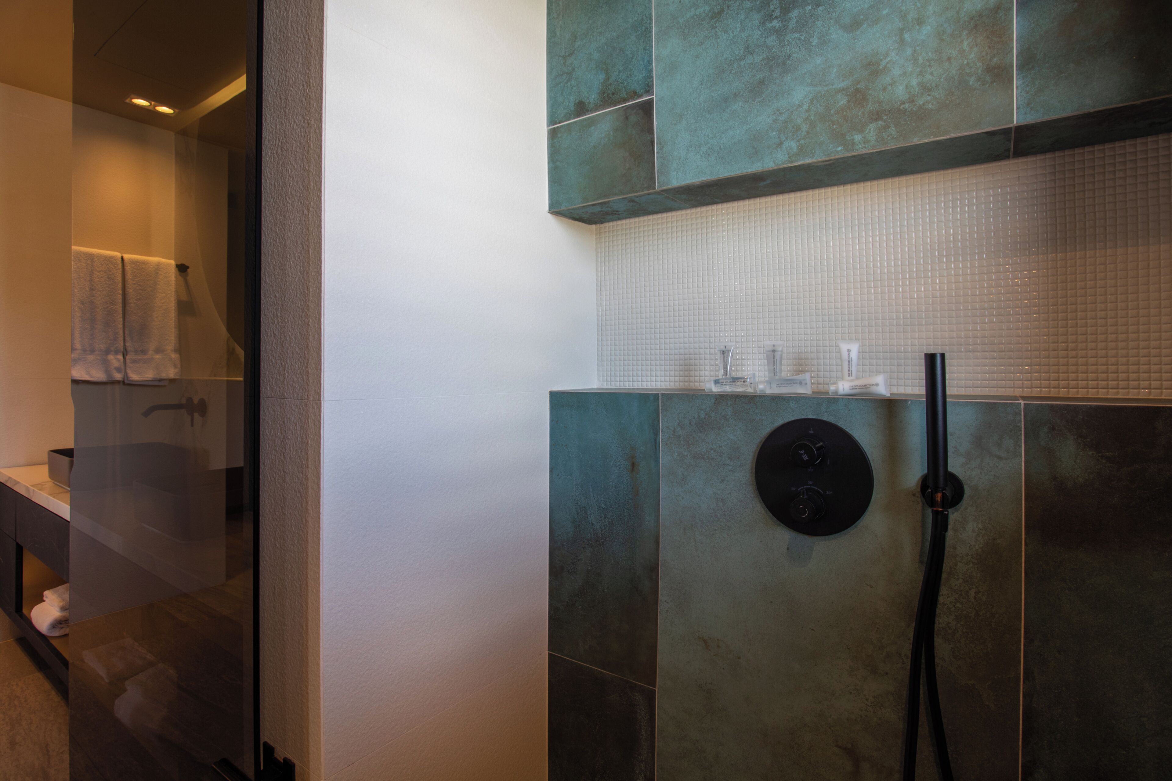 Un baño moderno con cabina de ducha de vidrio, un grifo redondo negro y una pared con azulejos.
