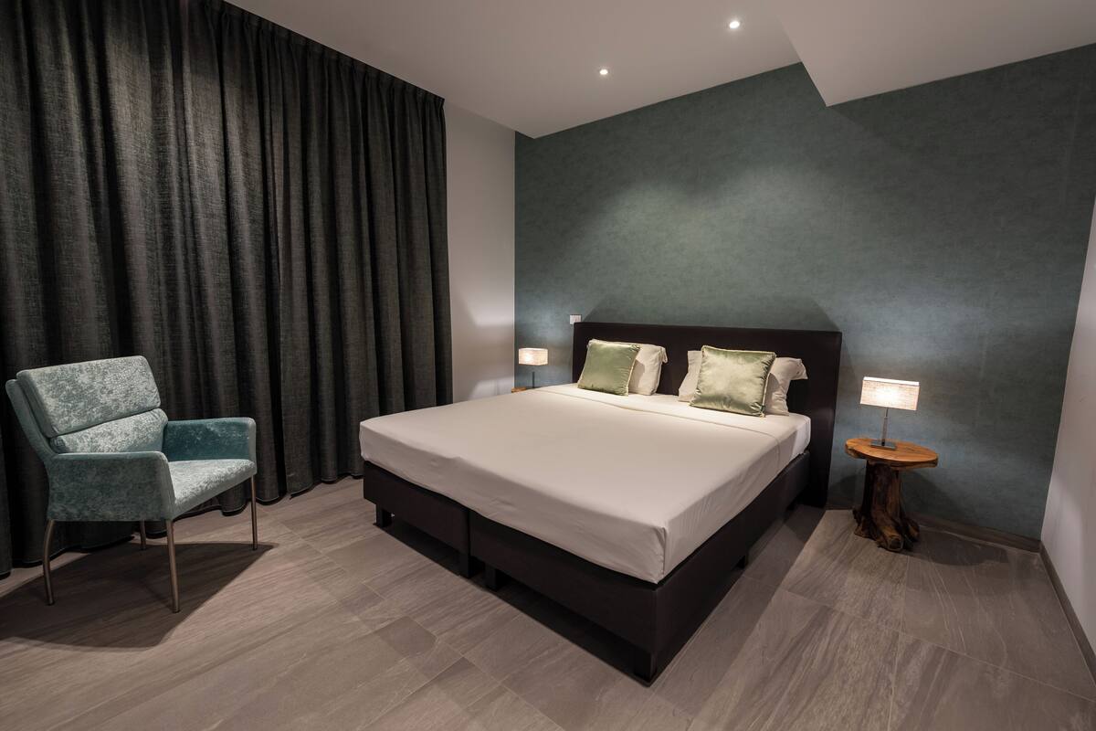 Un dormitorio moderno con una cama grande, una silla, una mesita de noche y una lámpara.
