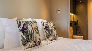 A hotel room with a bed, pillows with tropical prints, a shower area, and a control panel on the wall.