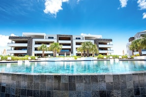 A modern hotel with a swimming pool, multiple balconies, and palm trees.