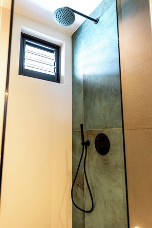 Ducha con cabezal de ducha de mano, ventana y panel de control en la pared.