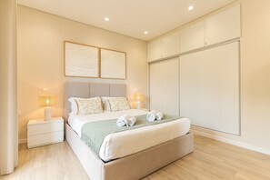 A hotel room with a bed, two bedside lamps, a headboard, a wall-mounted artwork, and a wardrobe.