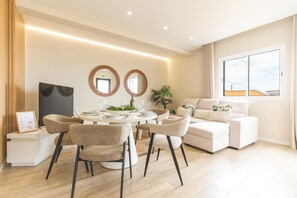 A modern living room with a dining area, featuring a sofa set, dining table, and two wall-mounted mirrors.