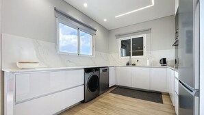 Een moderne keuken met een ingebouwde wasmachine, een groot raam en een roestvrijstalen koelkast.