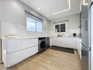 Eine moderne Küche mit Einbauwaschmaschine, großem Fenster und Edelstahl-Kühlschrank.