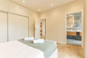 A bedroom with a bed, a bathroom with a mirror and sink, and a door leading to another room.