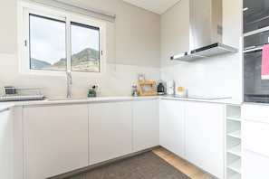 A modern kitchen with white cabinets, a window with a view of hills, and a stainless steel range hood.