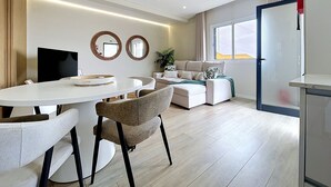 Een moderne woonkamer met een bank, een eettafel met stoelen, een televisie en twee spiegels aan de muur.