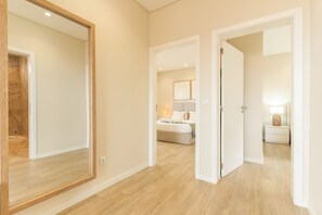 A hotel room with a large mirror, a bed with pillows, a bedside table with a lamp, and a nightstand.