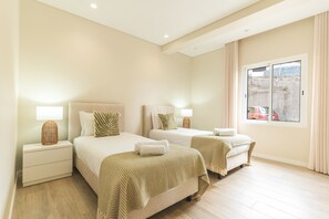 A hotel room with two beds, a nightstand with a lamp, a window with a view of a red car, and a curtain.