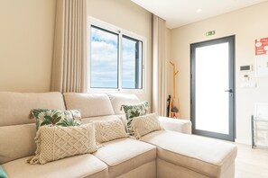 A living room with a sectional sofa, two macrame pillows, a window with curtains, and a door with an exit sign.