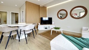 Een moderne woonkamer met een eethoek, een flatscreen televisie en twee spiegels aan de muur.